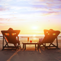 Two individuals reclining on lounge chairs at the beach during a glowing sunset, highlighting the calm that comes from safeguarding your family fortune across generations.