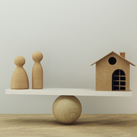 Wooden people figures and a small house balanced on a seesaw, symbolizing the delicate balance and control needed to manage family assets and secure family property