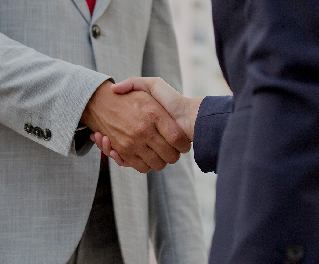 Two business professionals shaking hands, symbolizing partnership and collaboration in a professional setting, possibly related to multi-family offices and financial solutions