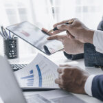 A professional businessperson uses a tablet to analyze financial data while reviewing printed charts and graphs. Streamlining compliance and unifying data for improved efficiency in family office operations.