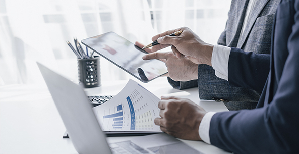 A professional businessperson uses a tablet to analyze financial data while reviewing printed charts and graphs. Streamlining compliance and unifying data for improved efficiency in family office operations.